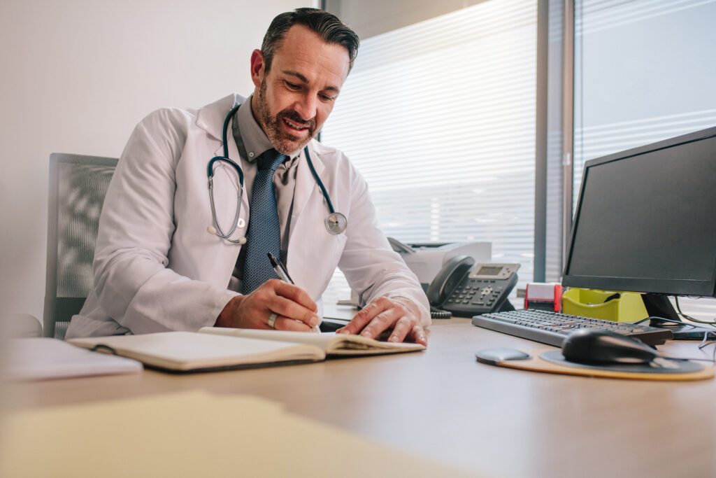 Male doctor writing on a notebook at his desk