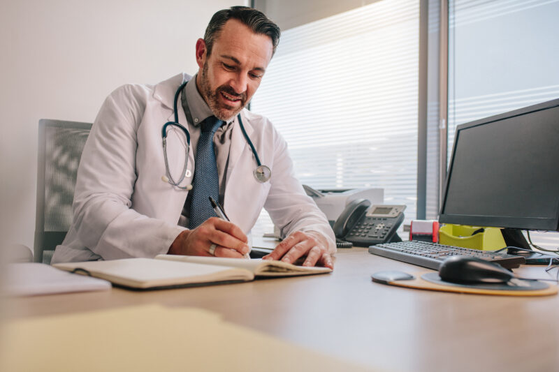 Male doctor writing on a notebook at his desk