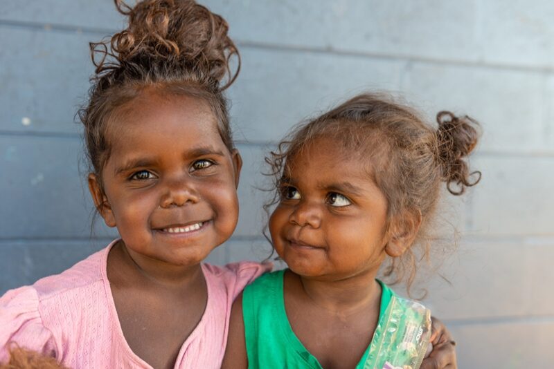 Two smiling aboriginal girls pictured in front of a wall