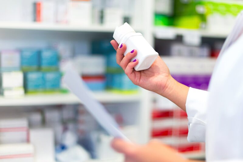 Image of hand of pharmacist holding medication bottle in a pharmacy