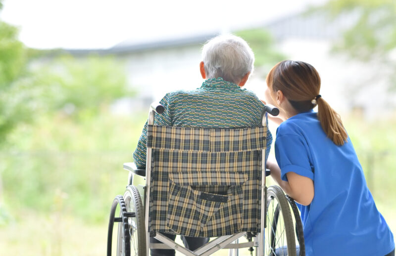 Elderly man in wheelchair with carer seated next to him