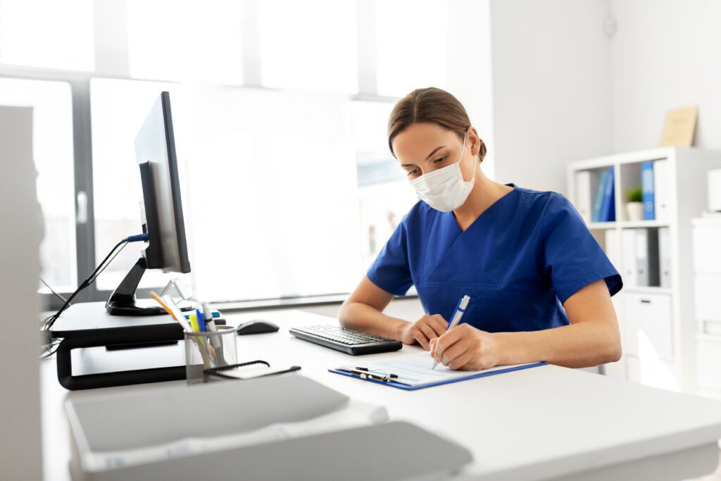 Health professional wearing mask sitting at computer wrtiting
