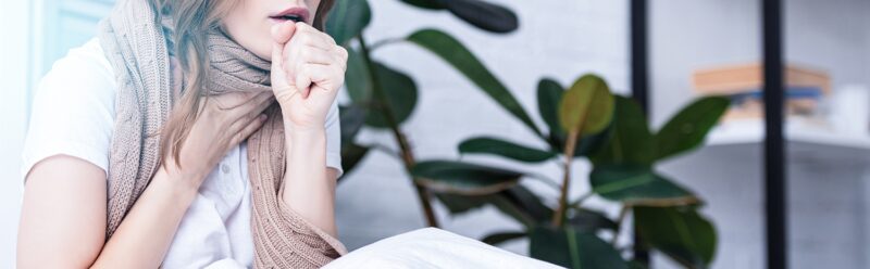 Image of woman coughing indoors while wearing a scarf