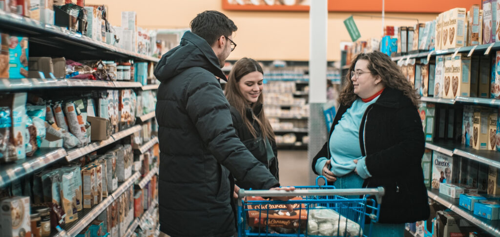 Three young people in a supermarket aisle with a trolley talking