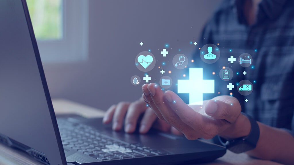 Hand holding digital health icons in front of laptop