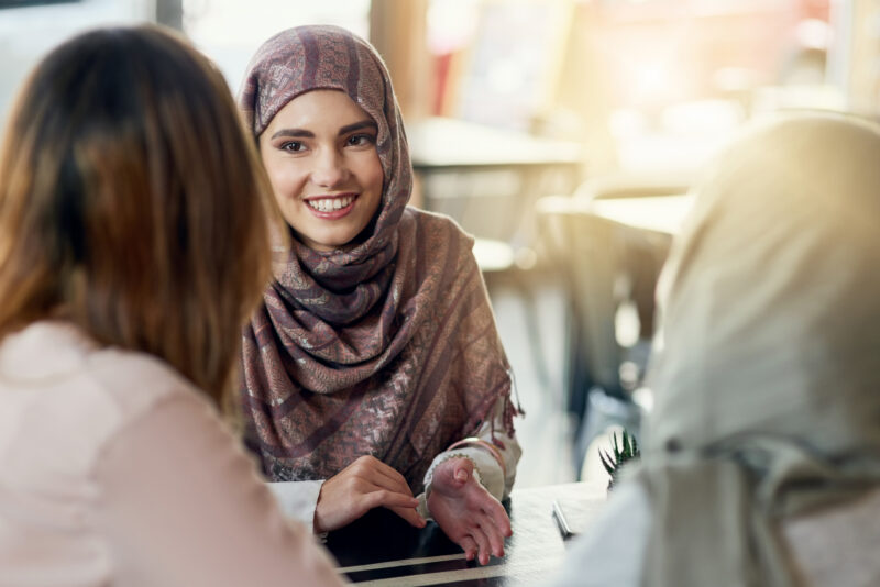 Friends, happy and Muslim women in cafe, bonding and talking together. Coffee shop, smile and Islamic girls, group or people chat, conversation and discussion for social gathering in restaurant