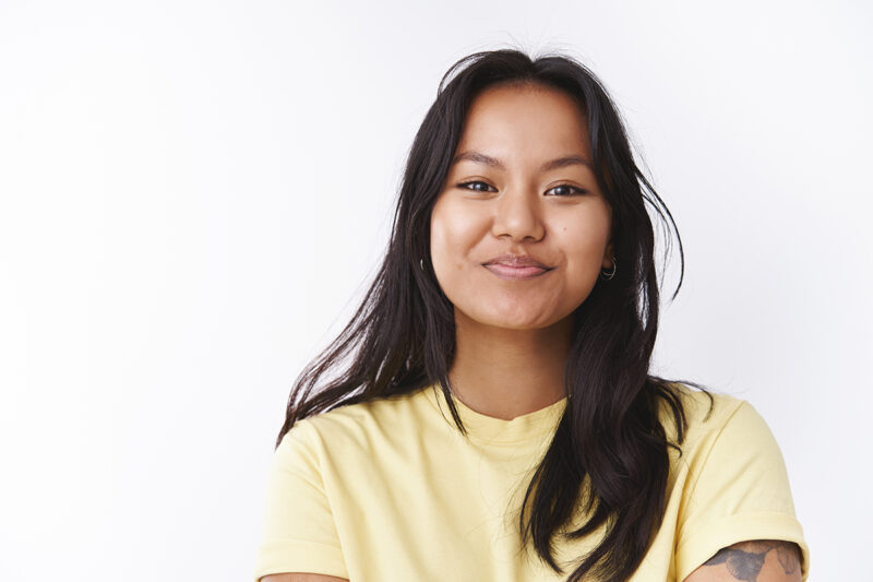 Close-up shot of amused enthusiastic good-looking malaysian woman with facial scars smiling feeling positive and optimistic grinning from happiness and good attitude over white background.