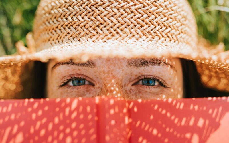 Woman in straw hat peering at the camera over a book