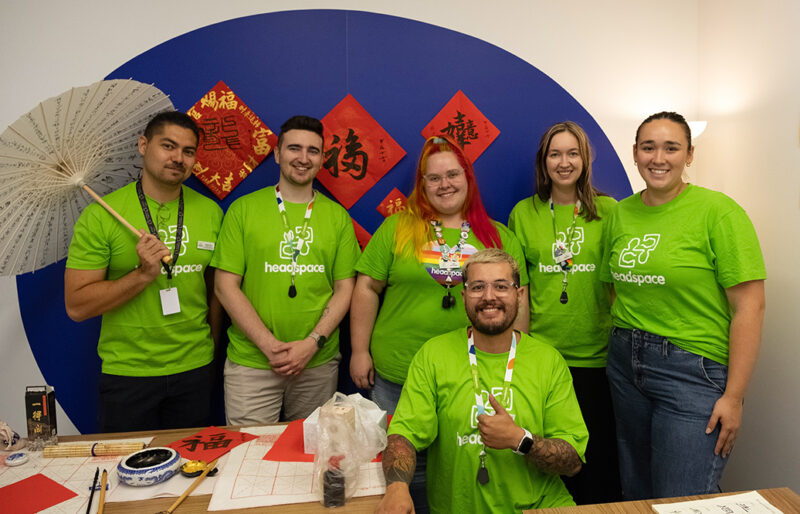 A team of six young adults in headspace green tshirts looking at camera in a room with asian decoration